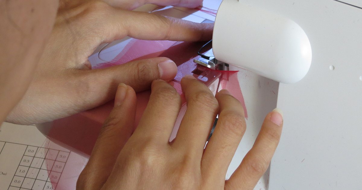 Manos que guían una tela bajo la aguja de una máquina de coser overlock