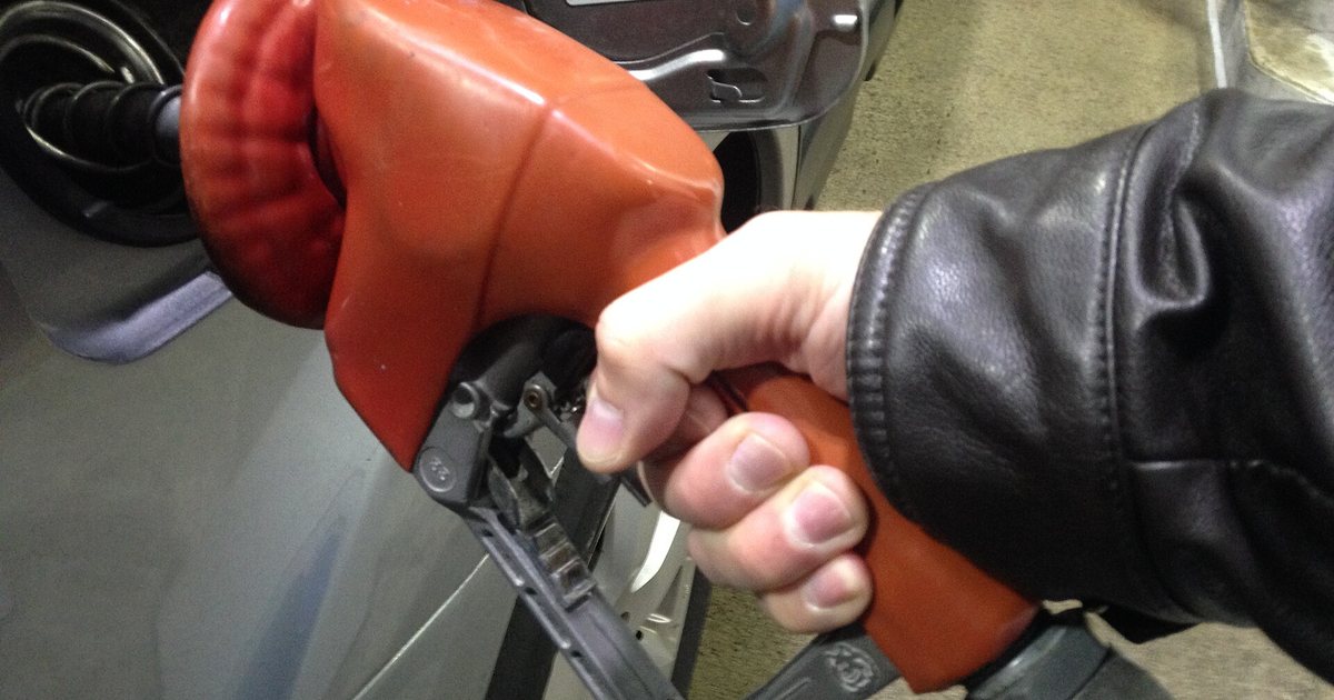 Una mano sostiene el pico del surtidor mientras carga combustible en el tanque de un auto