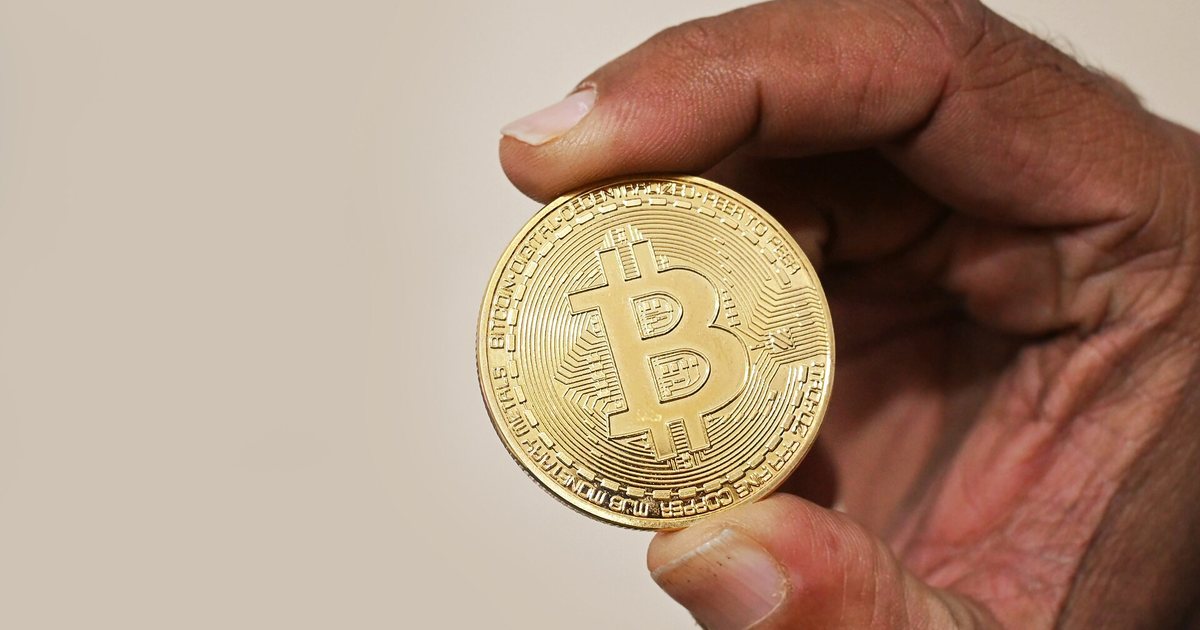Una mano sostiene una moneda física con el símbolo de bitcoin
