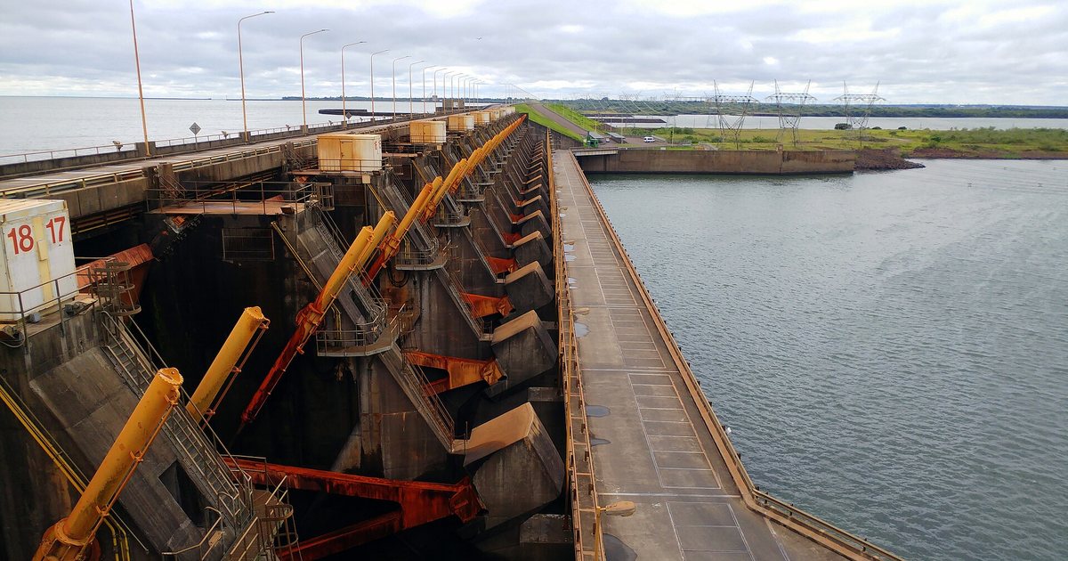 Compuertas y coronamiento de la represa de Yacyretá sobre el río Paraná, con torres de alta tensión al fondo