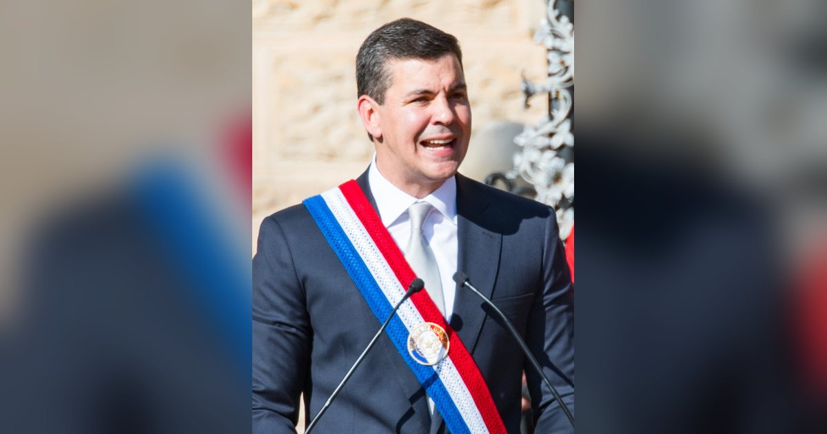 El presidente Santiago Peña, con la banda presidencial, habla ante un micrófono en Asunción