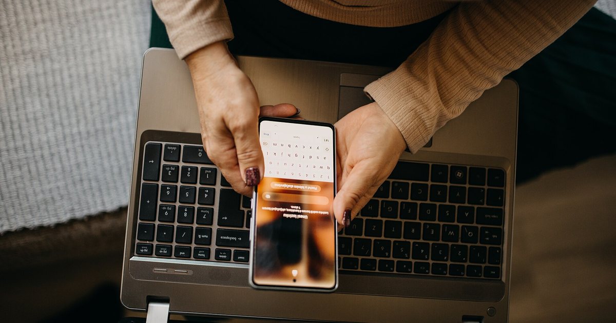 Manos de una mujer que usa el celular sobre una computadora portátil