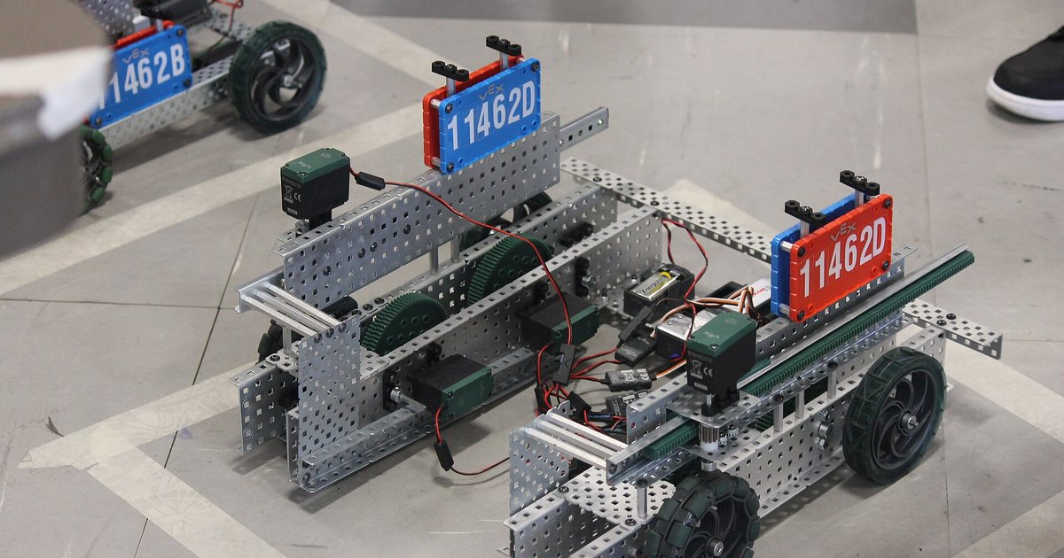 Robots armados con piezas metálicas, ruedas y cables de un kit de robótica educativa, sobre el piso de una competencia